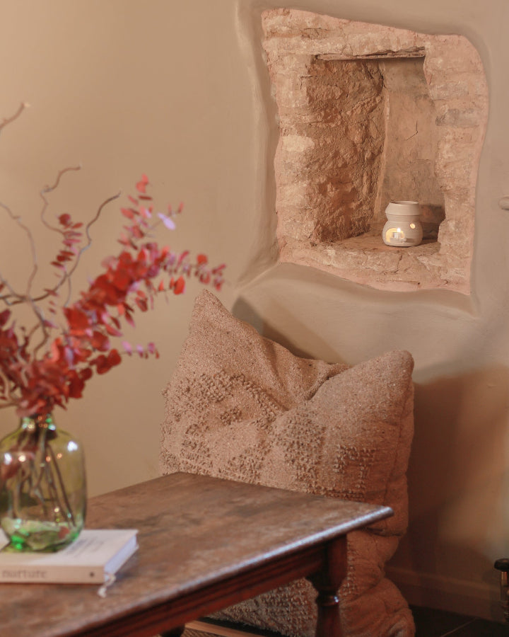wax burner with a lit tea light candle inside, sitting on a stone shelf.