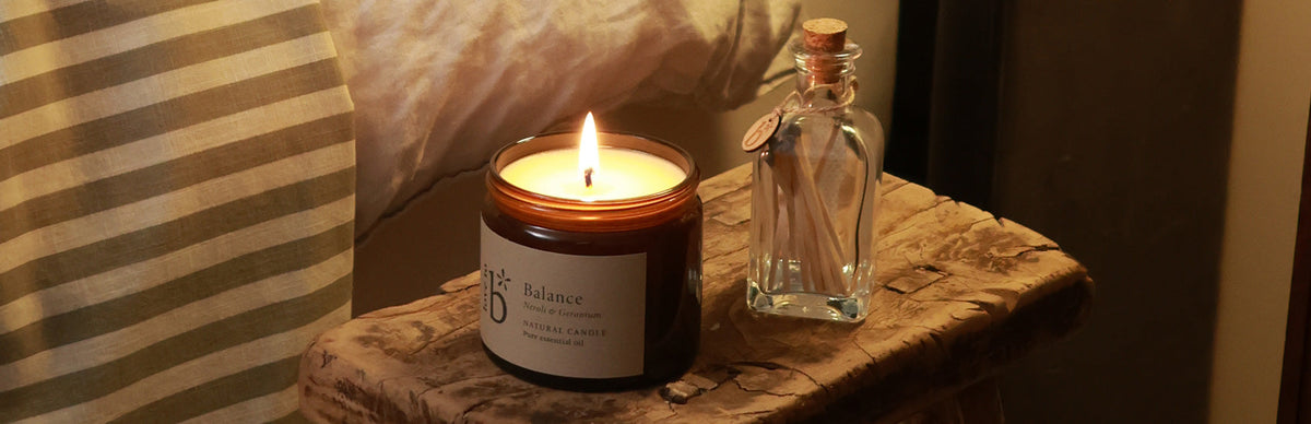 A natural soy candle and matches in a jar made by Love to b, sitting next to a bed on a stool in the bedroom