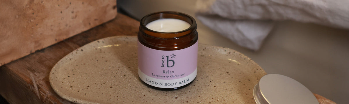 Love to b natural hand and body balm on a plate next to a bed with the lid off