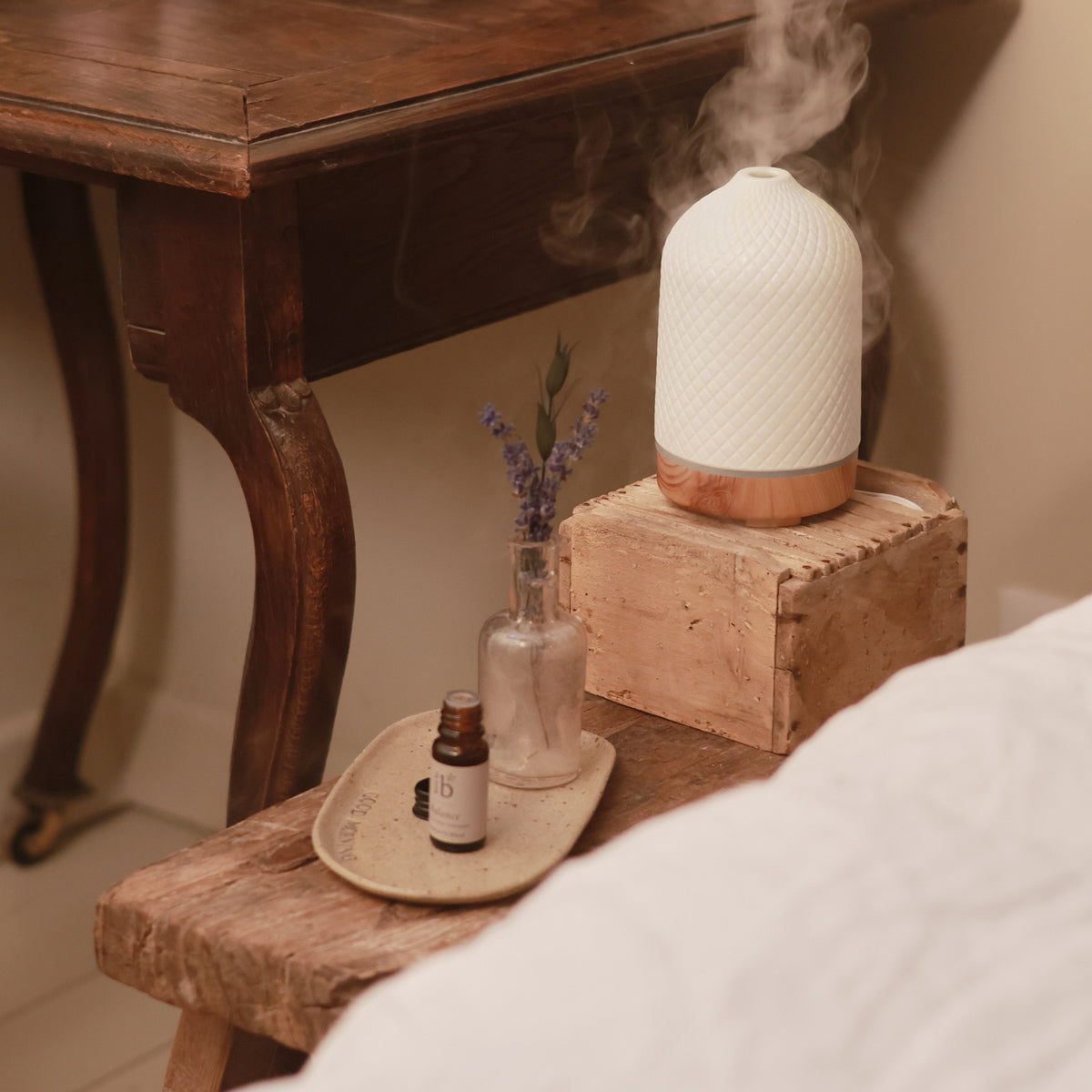 Room diffuser sitting on a side table with a bottle of natural essential oil