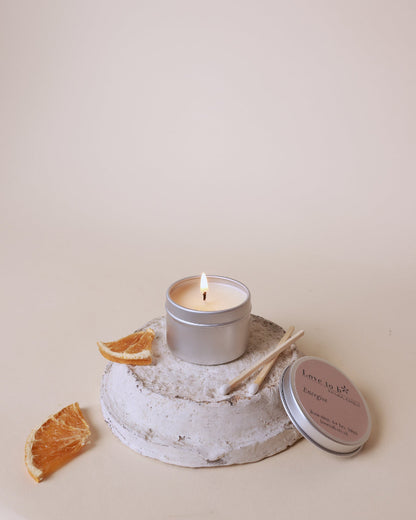A lit natural candle tin sits on a painted pot with two matches and dried orange next to it.