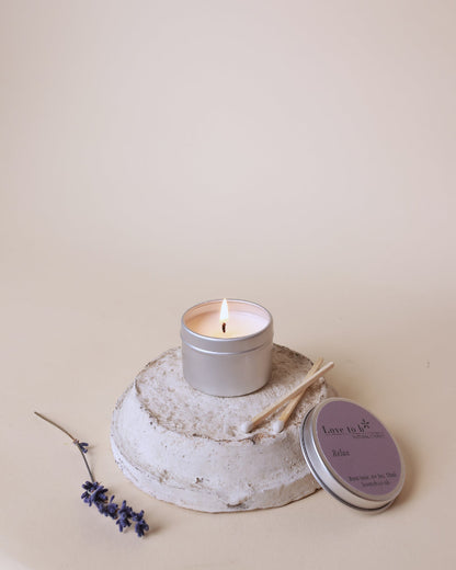 A lit natural soy candle tin from Love to b sits on a painted pot with some lavender next to it.