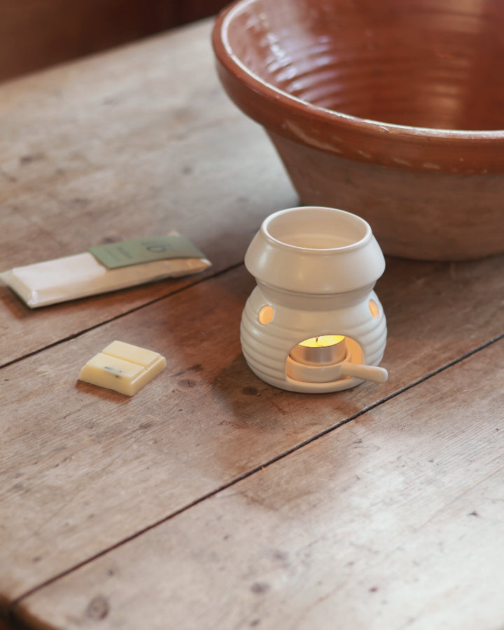 soy wax bars on a wooden surface next to a lit wax burner and a ceramic pot in the background.