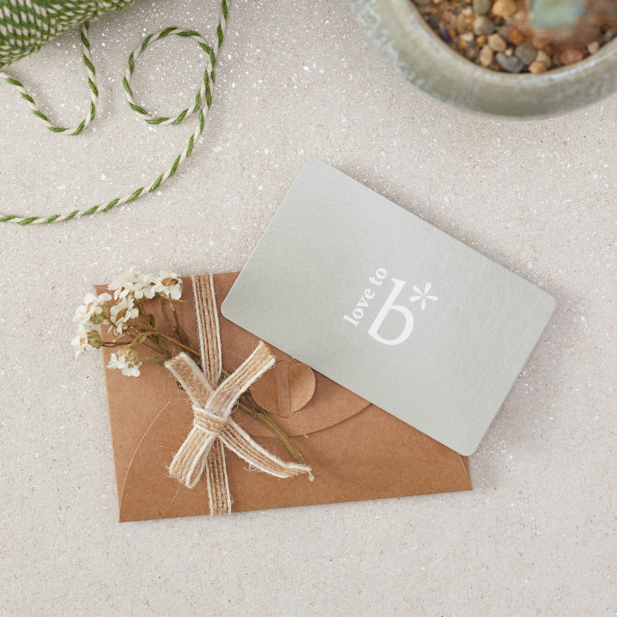 A physical gift card from Love to b, placed on a craft paper envelope, tied with a burlap ribbon, with decorative dry flowers attached to the envelope. 